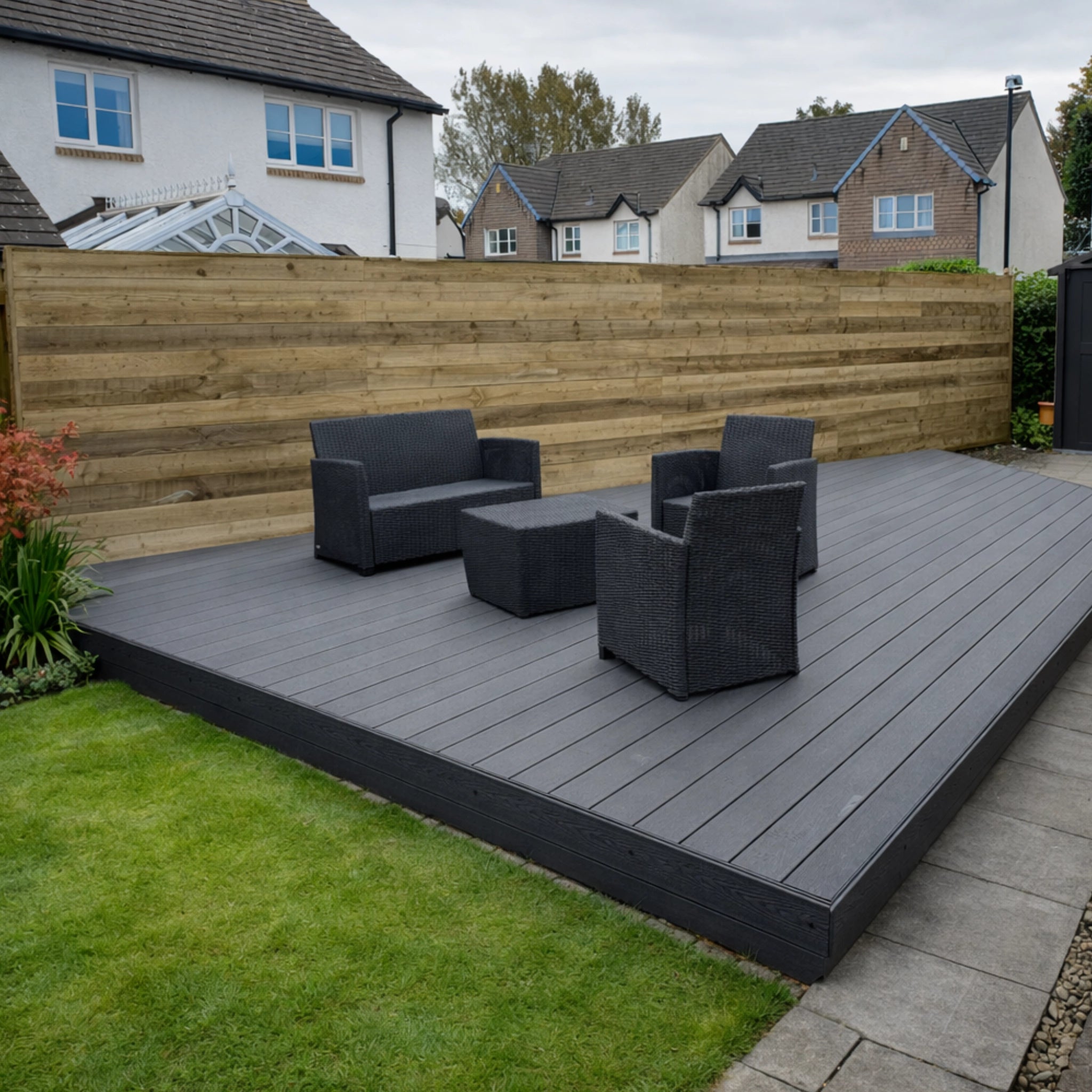 Gray deck with black outdoor furniture in a residential backyard.