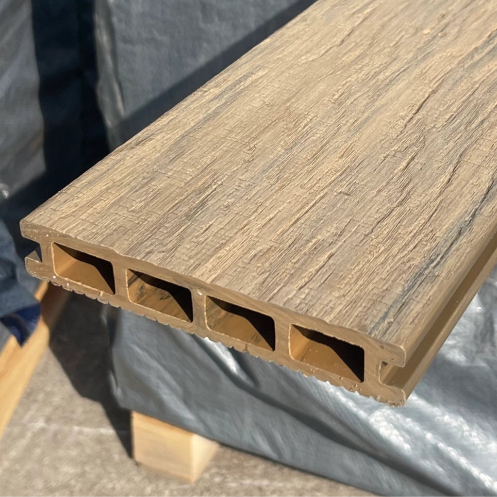 Close-up of a beige composite deck board with a gray tarp in the background