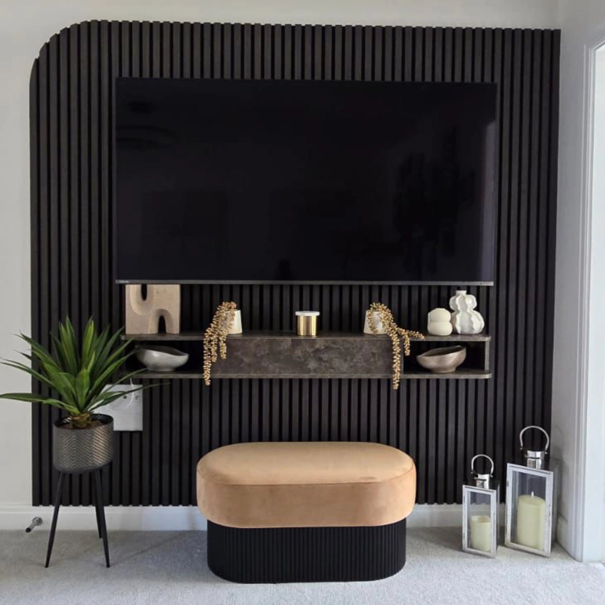 Modern living room with a black oak acoustic wall panelled wall, beige ottoman, and decorative items.