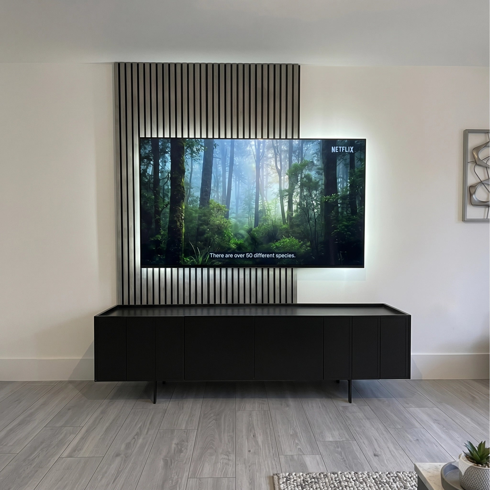 Modern living room with a large TV displaying a nature scene, with concrete acoustic wall panel background placed above a black entertainment console.