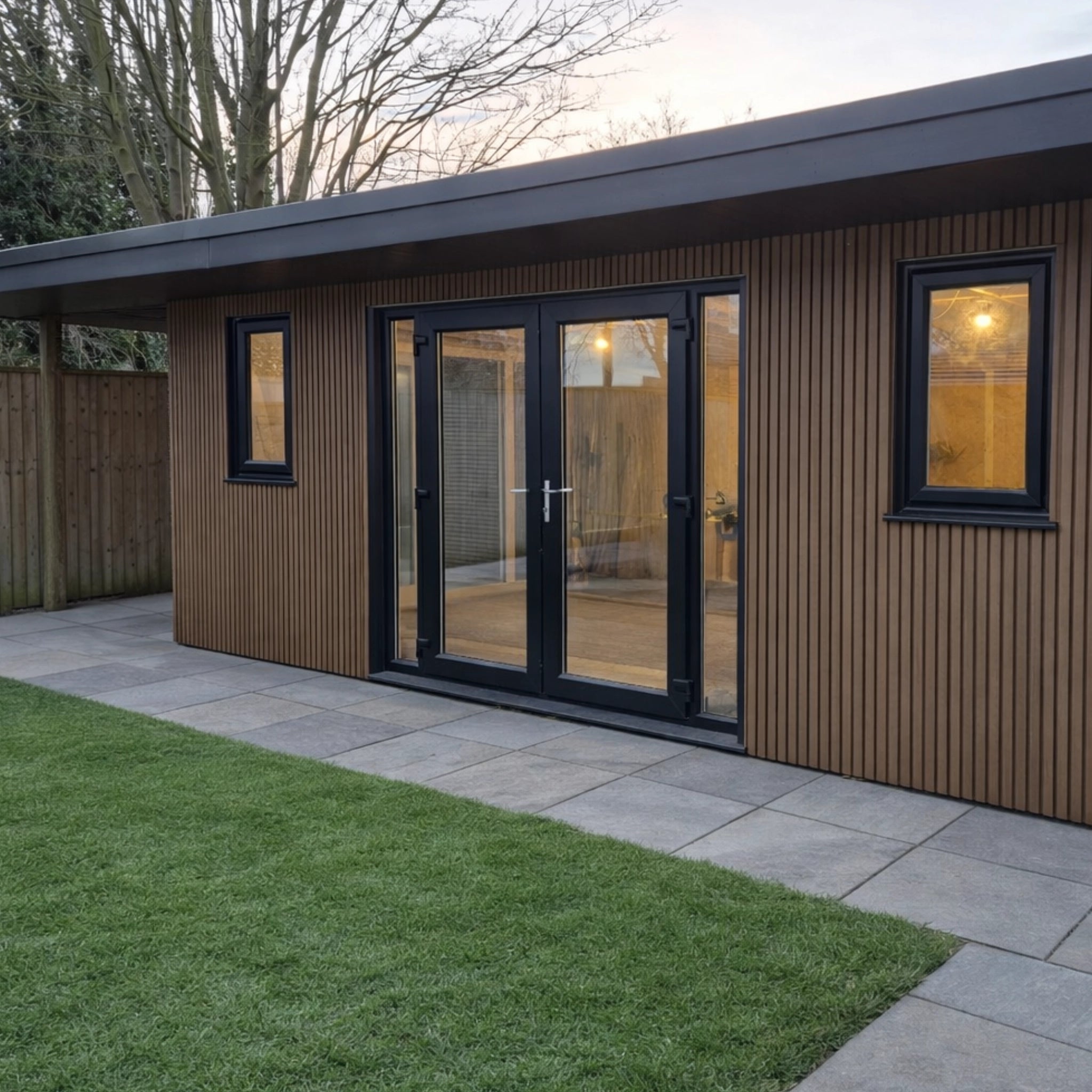 Modern garden building with teak co-extrusion composite cladding exterior and glass doors, surrounded by grass and pavement.