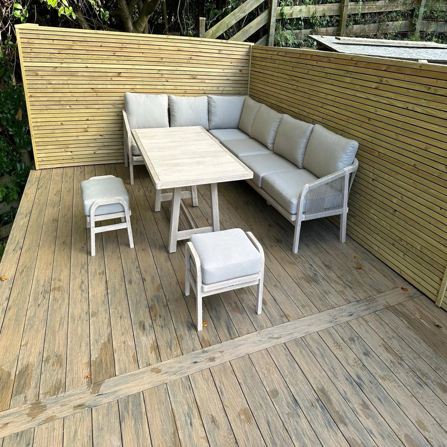 Outdoor furniture set on a beige driftwood composite decking with a wooden wall in the background.