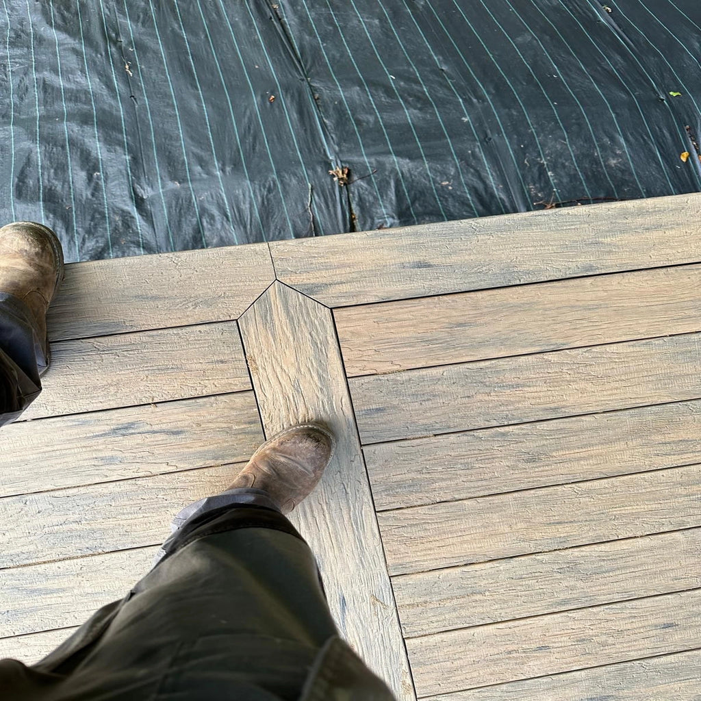 Person walking on a beige driftwood composite decking with a dark water body in the background