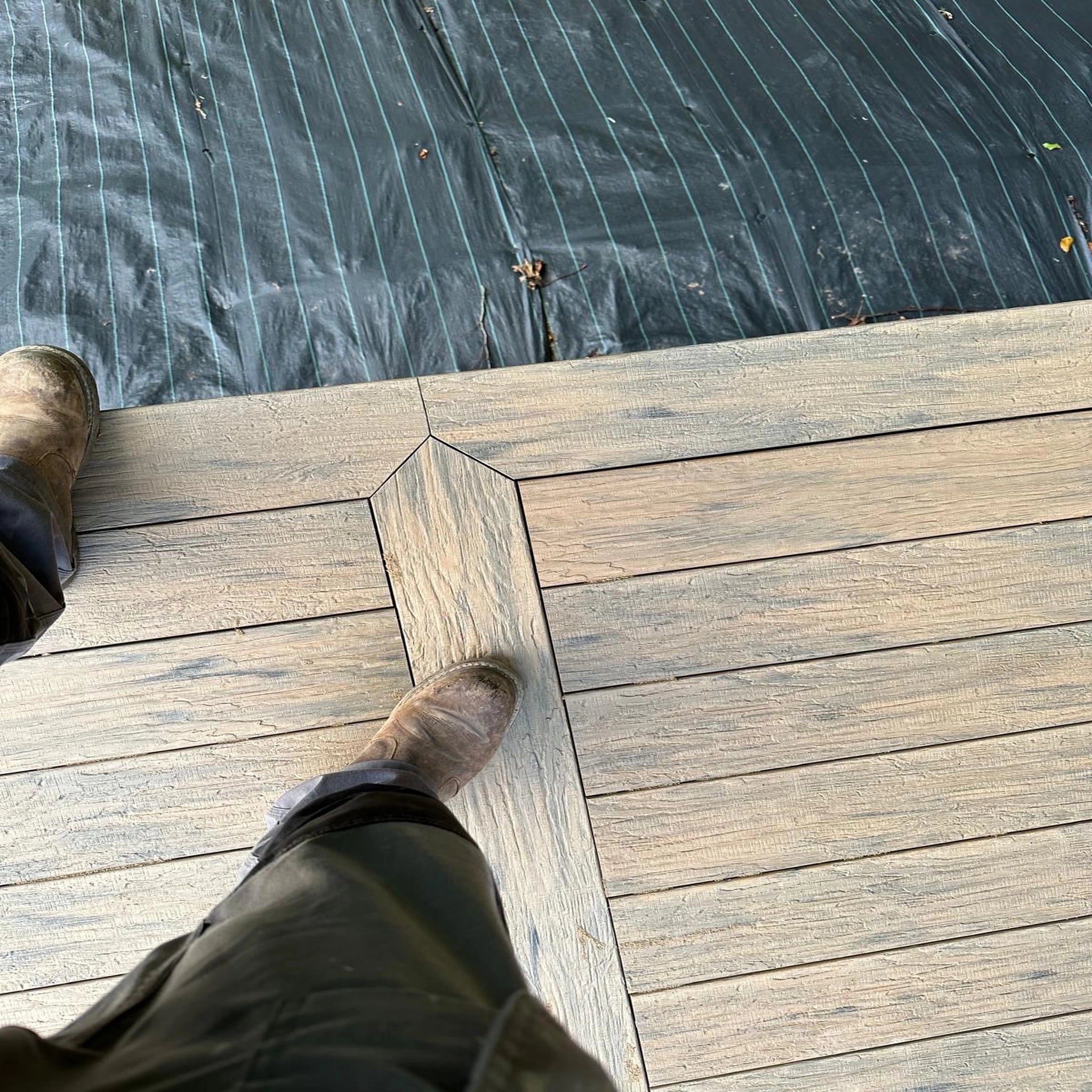 Person walking on a beige driftwood composite decking with a dark water body in the background