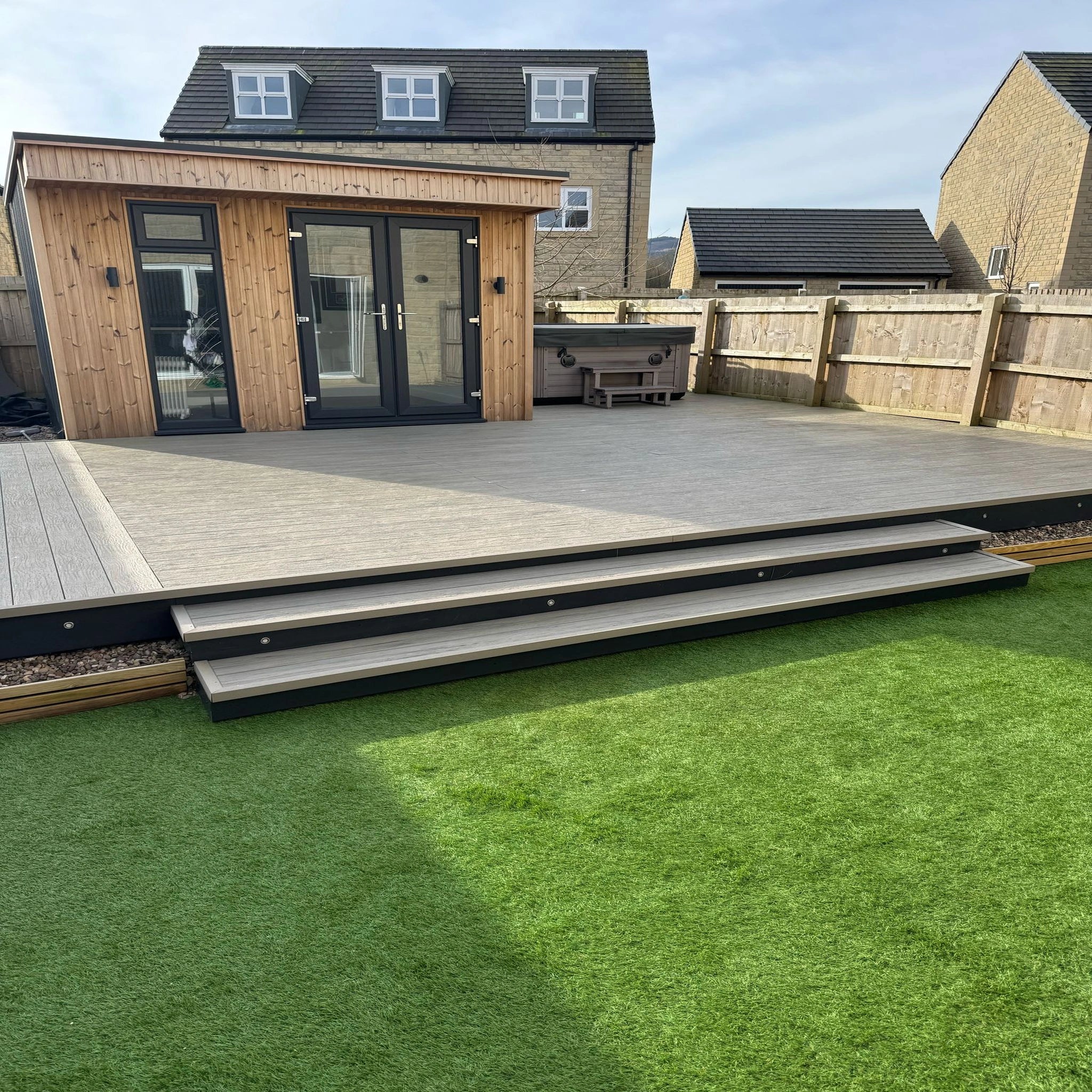Outdoor grey driftwood composite deck area with wooden structure and steps leading to a house.