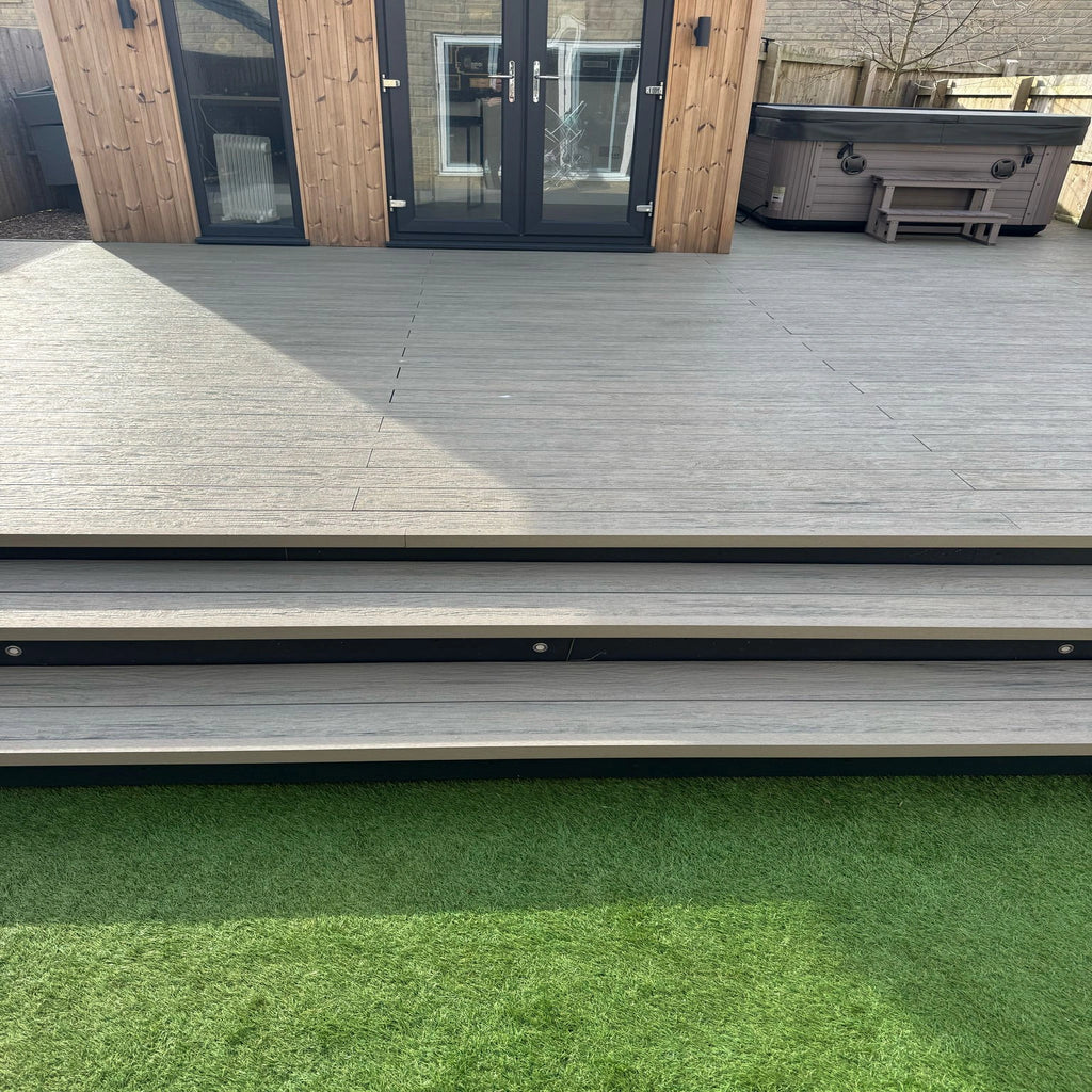 grey driftwood composite deck with steps leading to a patio area with a hot tub.