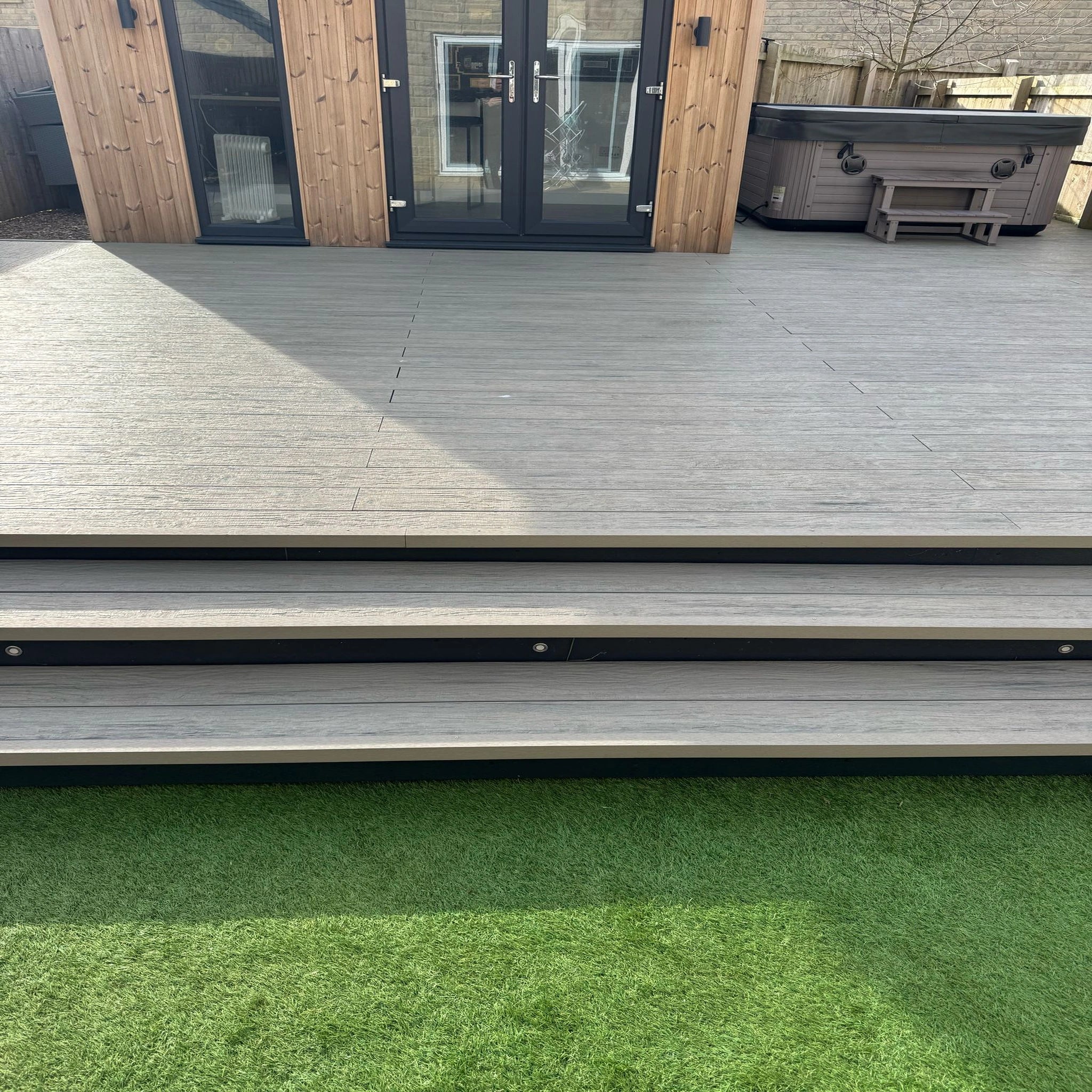 grey driftwood composite deck with steps leading to a patio area with a hot tub.