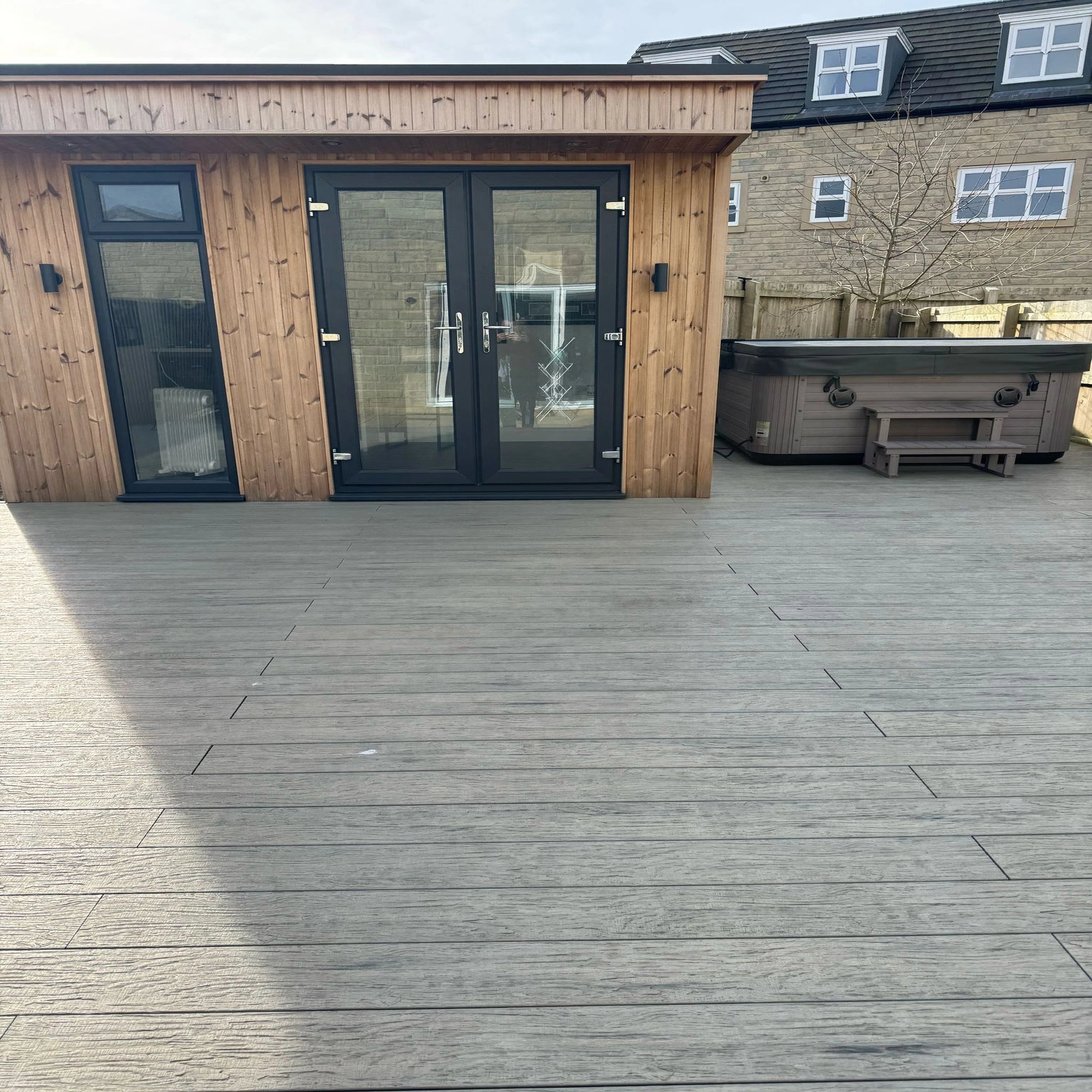 grey driftwood composite deck with a wooden cabin and hot tub in the background
